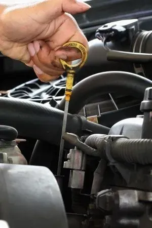 Hand holding a yellow dipstick above an engine bay, checking engine oil. | Sparks Tire & Auto