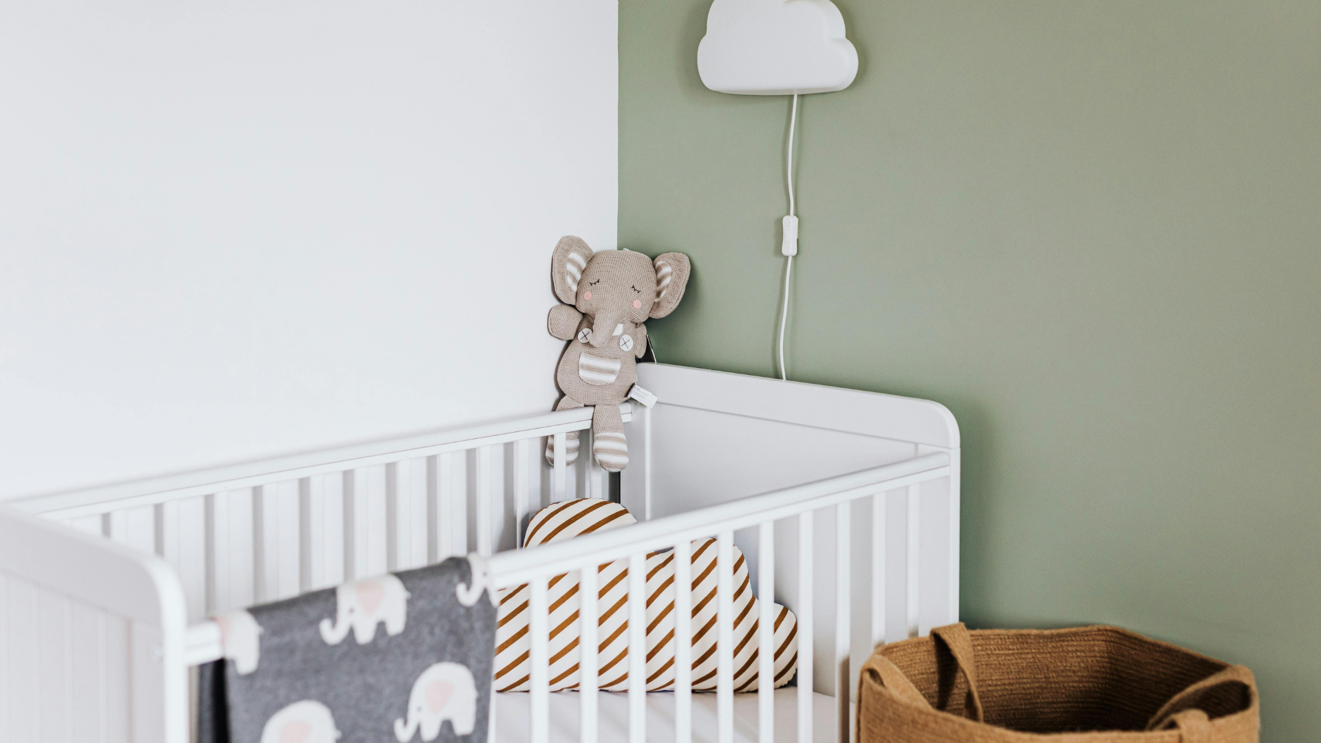White crib with elephant-themed decor in a nursery with light green and white walls.
