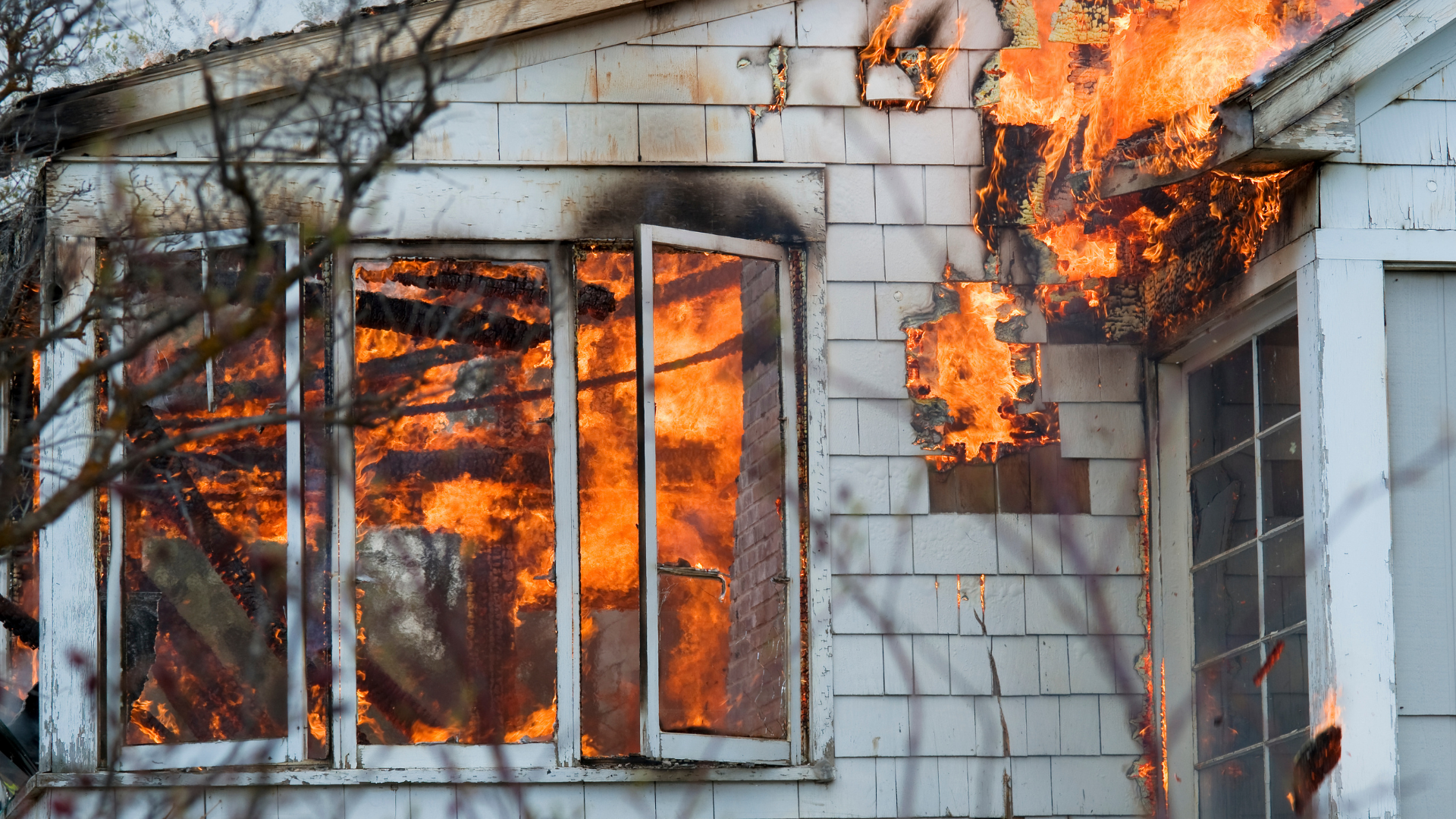House engulfed in flames, fire bursting from windows and siding.