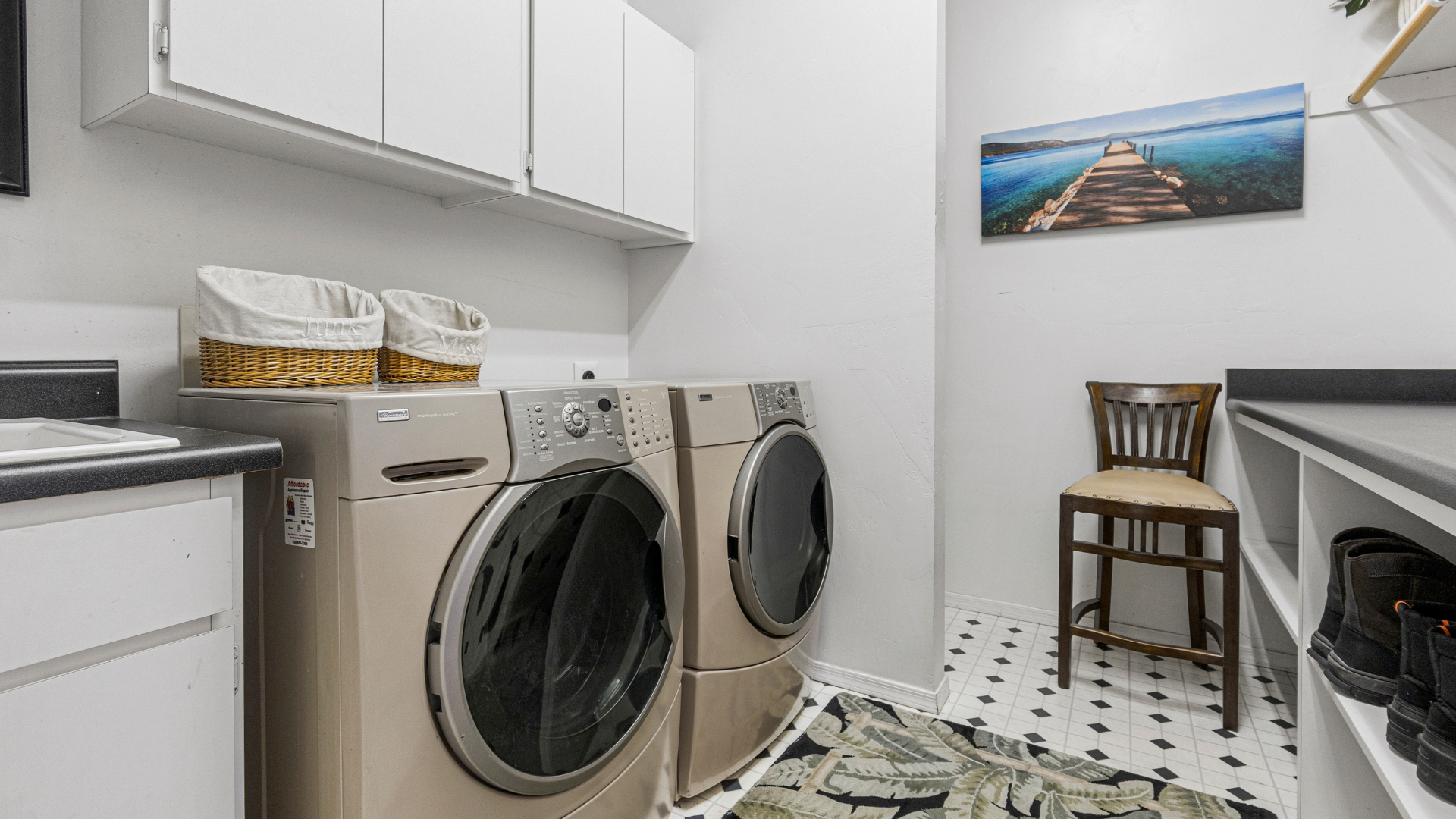 Laundry room with stacked washer and dryer, white cabinets, and a chair by a counter.