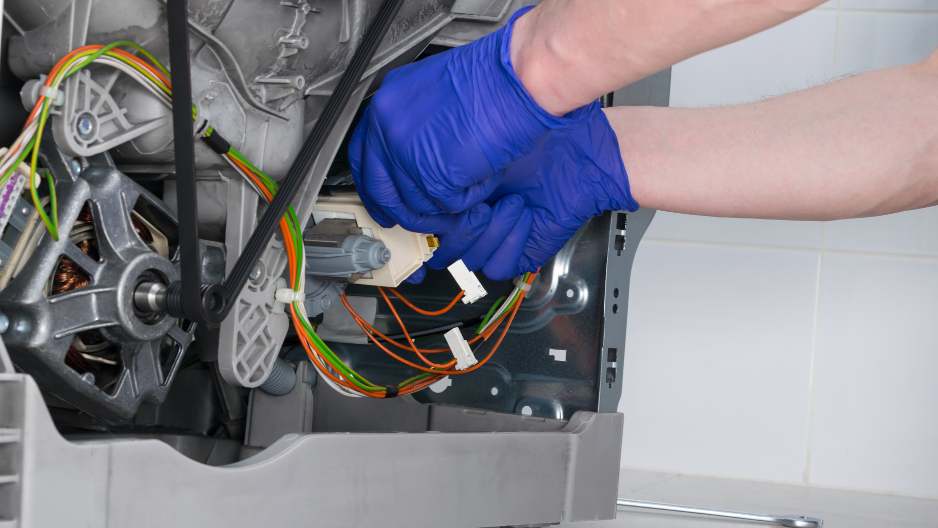 Person in blue gloves working on the inner components of a washing machine.