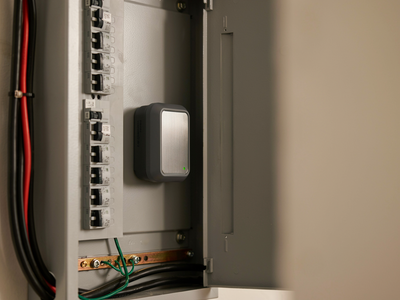Electrical panel with circuit breakers and a small device mounted inside, with red and black wires visible.