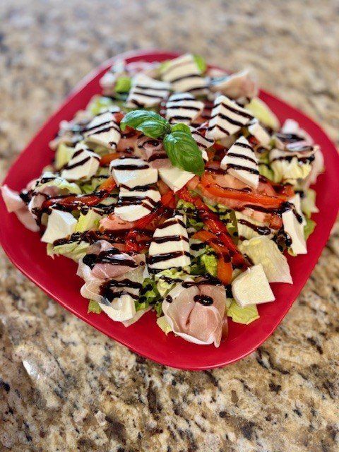 Salad with mozzarella, tomatoes, prosciutto, and balsamic glaze on a red plate.