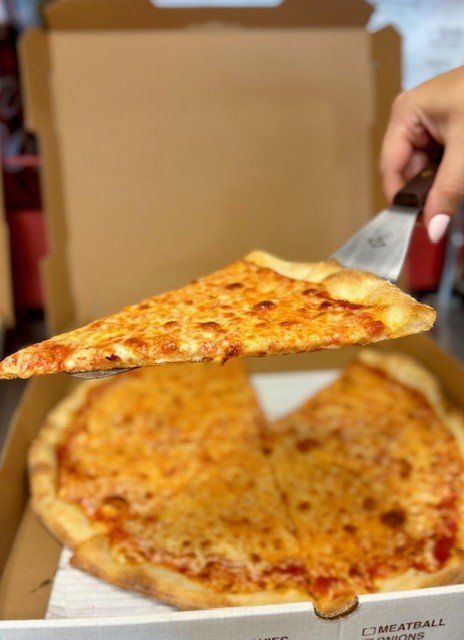 A hand holding a slice of cheesy pizza above a pizza box.