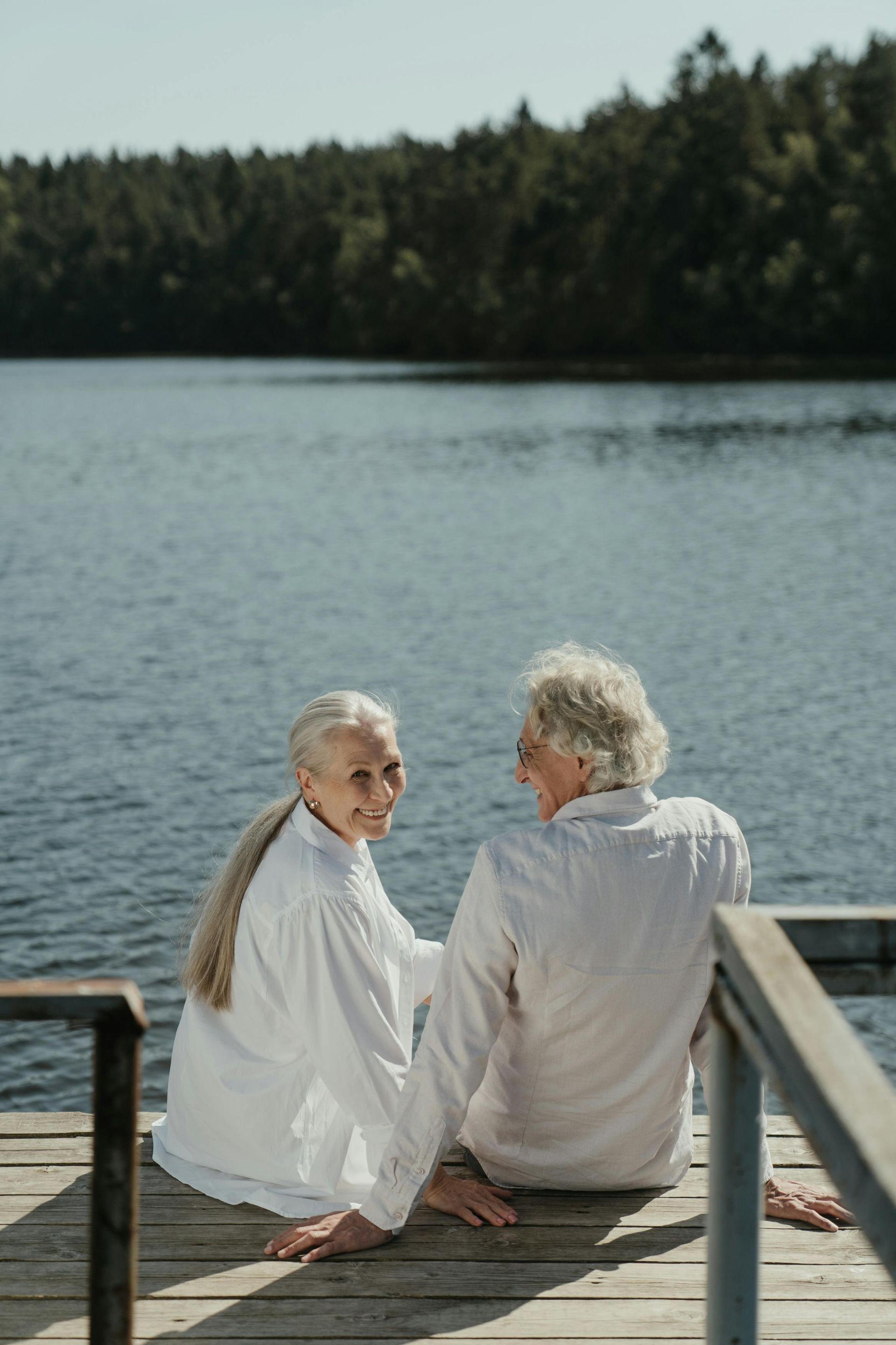 An elderly couple is sitting on a dock looking at a lake.