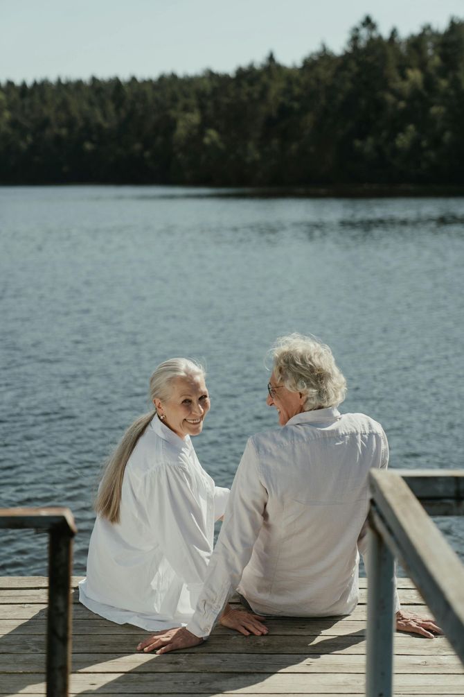 An elderly couple is sitting on a dock looking at a lake.