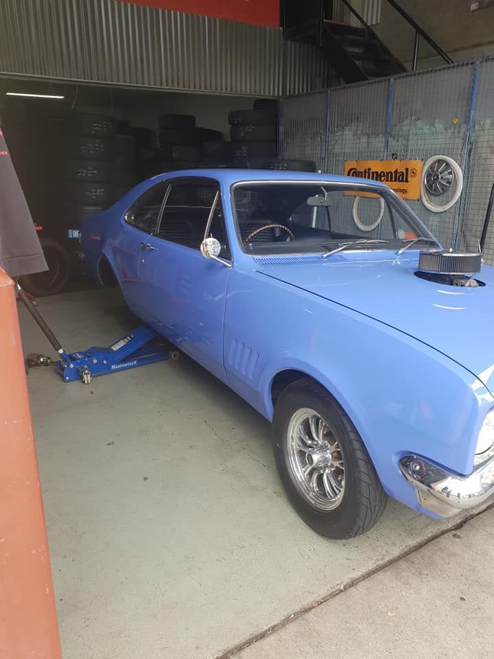 A blue car is sitting on a jack in a garage. — Budget Tyre Shed In Charmhaven, NSW