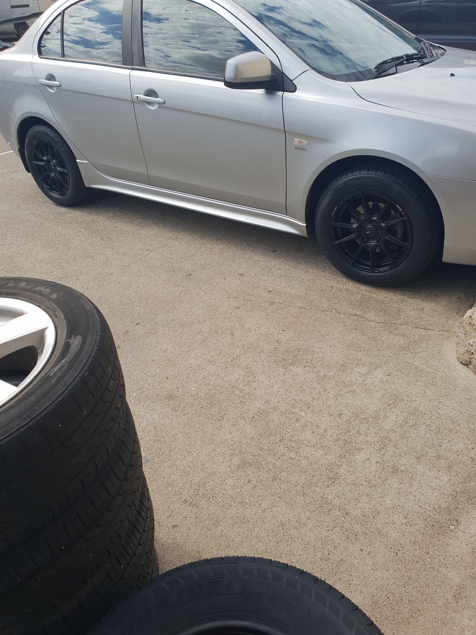 A silver car is parked next to a pile of tires. — Budget Tyre Shed In Charmhaven, NSW