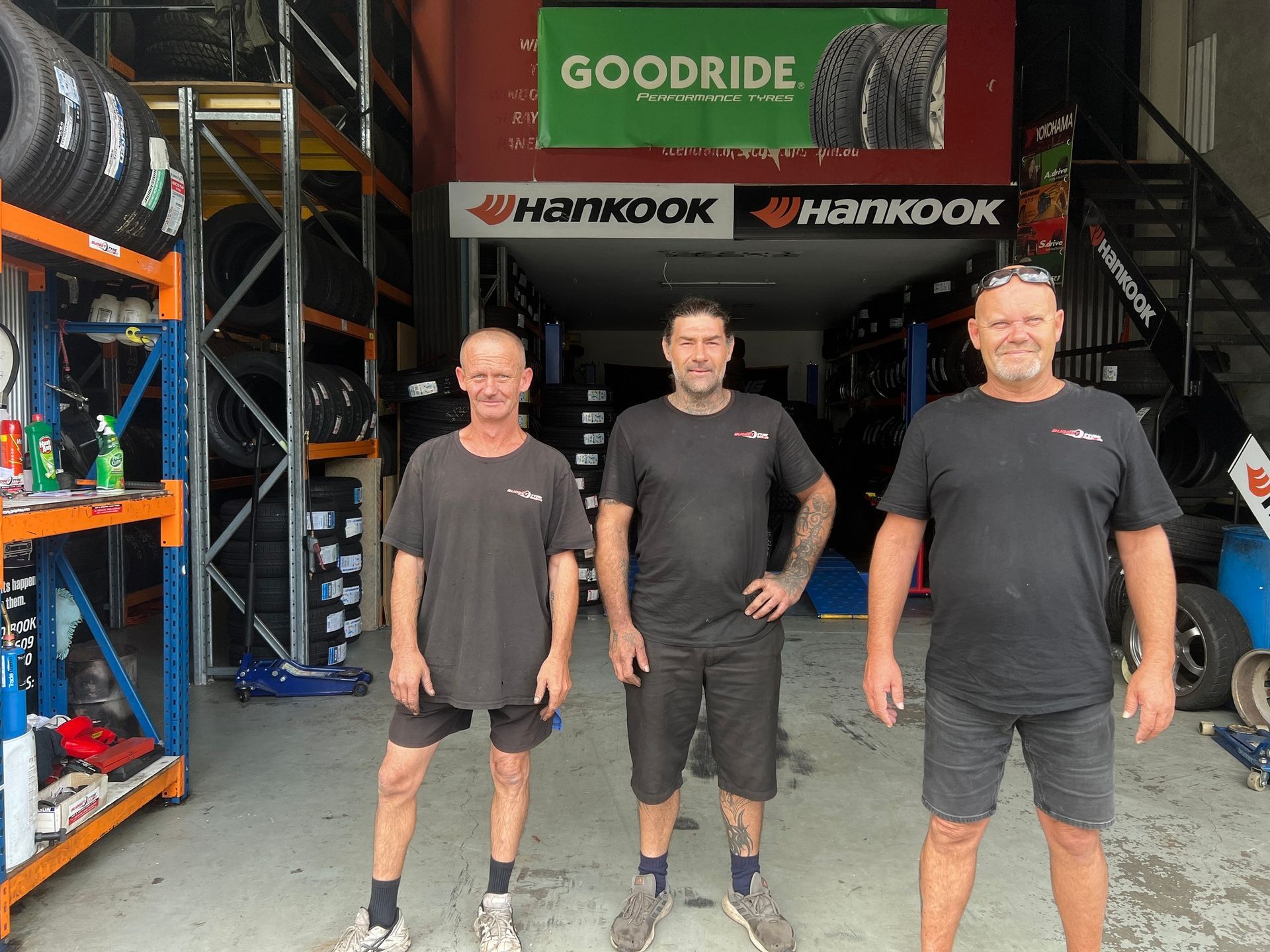 Three men are standing in front of a tire store. — Budget Tyre Shed In Charmhaven, NSW
