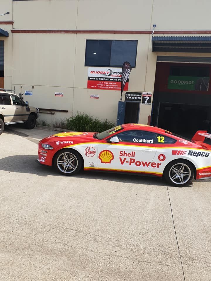 A Red and White Race Car driving in Front of A Building — Budget Tyre Shed In Charmhaven, NSW