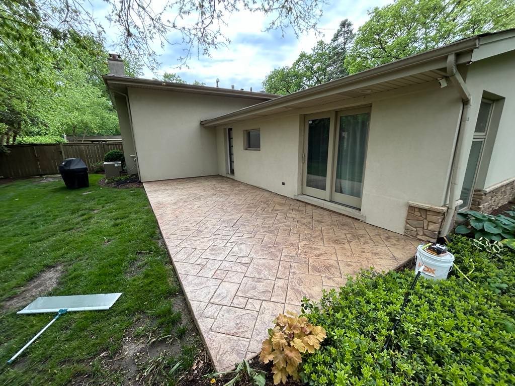 Picture of a backyard patio during a Soft Washing service in Highland Park, Illinois, showing a large stamped concrete patio beside a residential home with freshly cleaned surfaces and surrounding green landscaping.