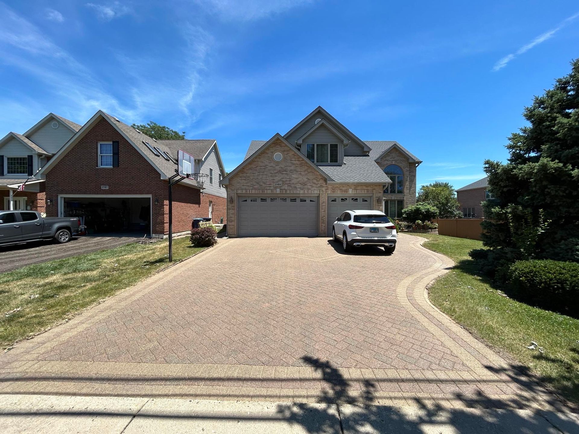 You can see an image of a residential brick-paver driveway during a Soft Washing service in Highland Park, Illinois, featuring a large suburban home with a freshly cleaned driveway, parked vehicle, and bright blue sky in the neighborhood setting.