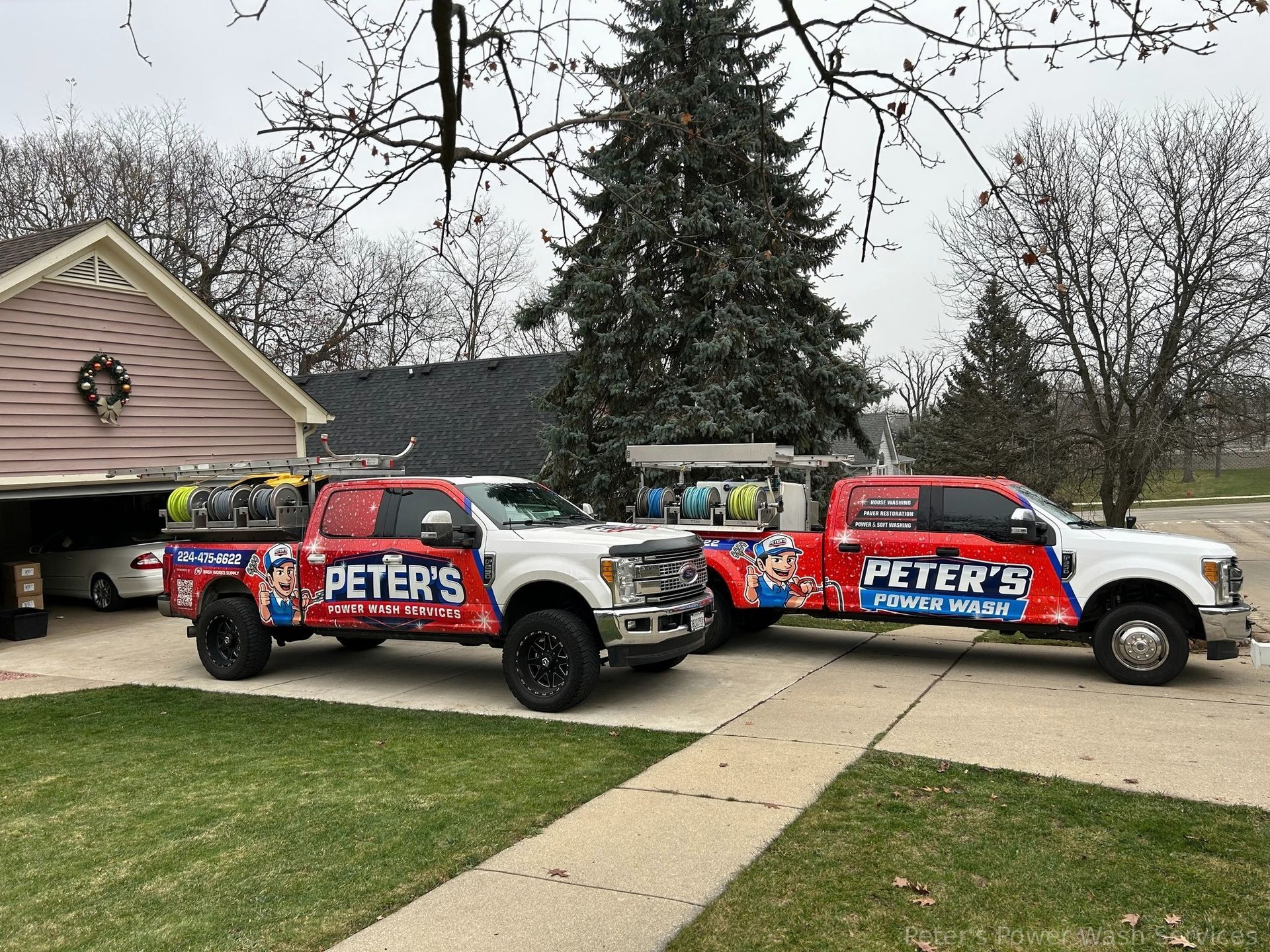 Image of two Peter Power Washing service trucks parked in a residential driveway in Glencoe, Illinois, prepared for Power Wash Services in Glencoe with trees and suburban homes visible in the background.
