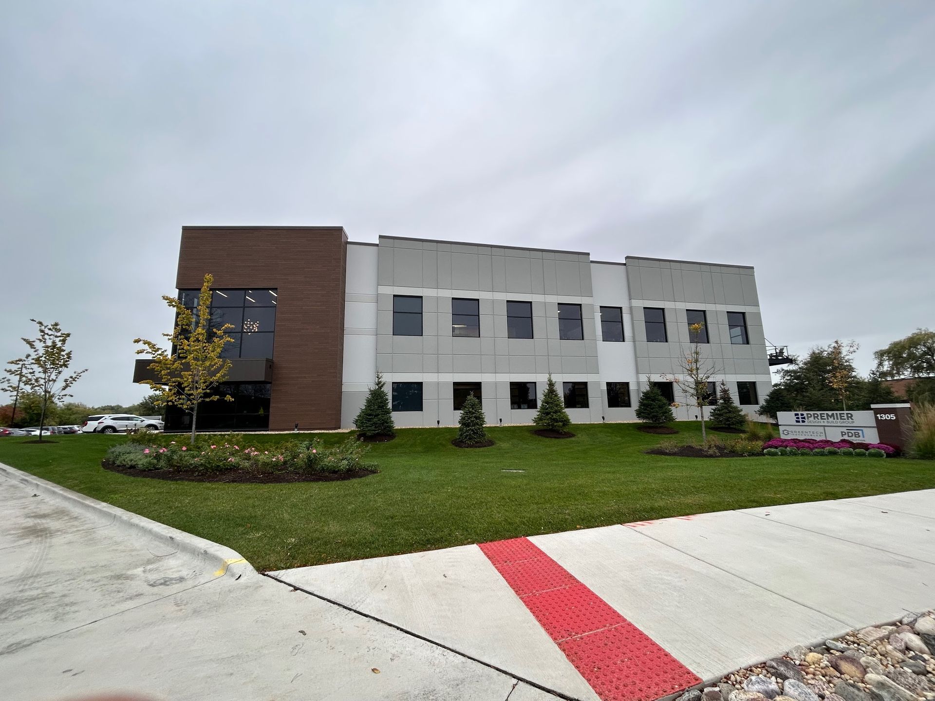 Image of a modern commercial office building during a Soft Washing Commercial Exterior Cleaning service, featuring freshly cleaned white exterior walls, landscaped greenery, and a wide concrete sidewalk under a cloudy sky.