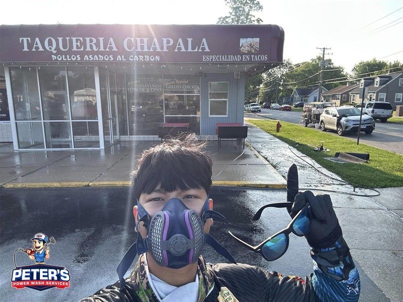 Picture of a worker standing in front of a commercial storefront during a Soft Washing house and building wash service in Cary, Illinois, wearing protective gear and holding cleaning equipment while freshly cleaned sidewalks and parking areas are visible outside the restaurant.