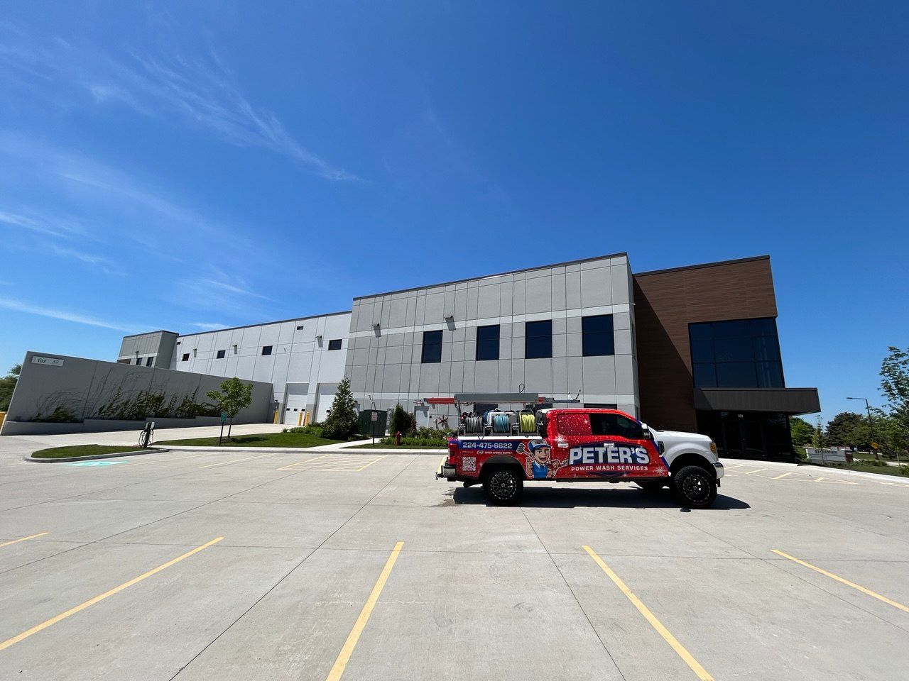 Picture of a large commercial property during a Soft Washing Building Cleaning service, featuring a Peter Power Washing truck parked outside a modern industrial building with freshly cleaned concrete and exterior walls under a bright blue sky.