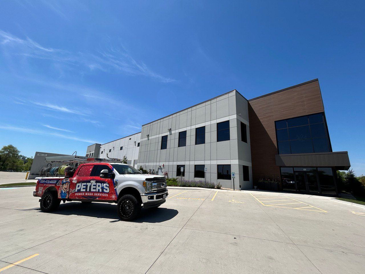 Image of a large modern commercial building during a Pressure Washing service in Highland Park, Illinois, with a Peter Power Washing truck parked in the empty lot under a bright blue sky beside the freshly cleaned exterior.