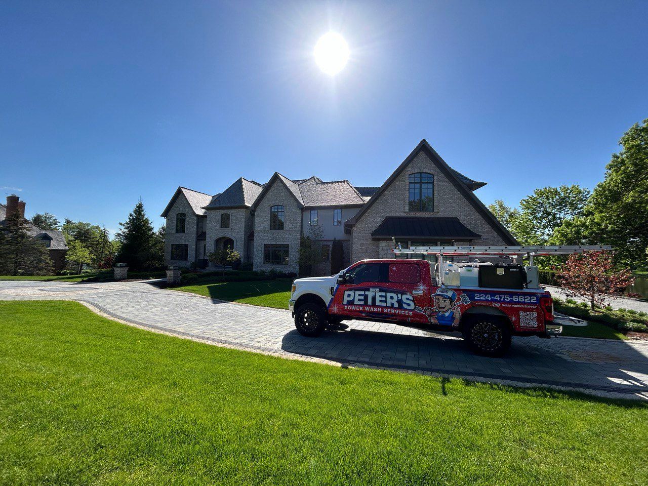 Picture of a Peter Power Washing truck parked outside a large residential property during an HOA Power Washing service, showing a clean driveway and neatly maintained lawn beneath bright sunlight.