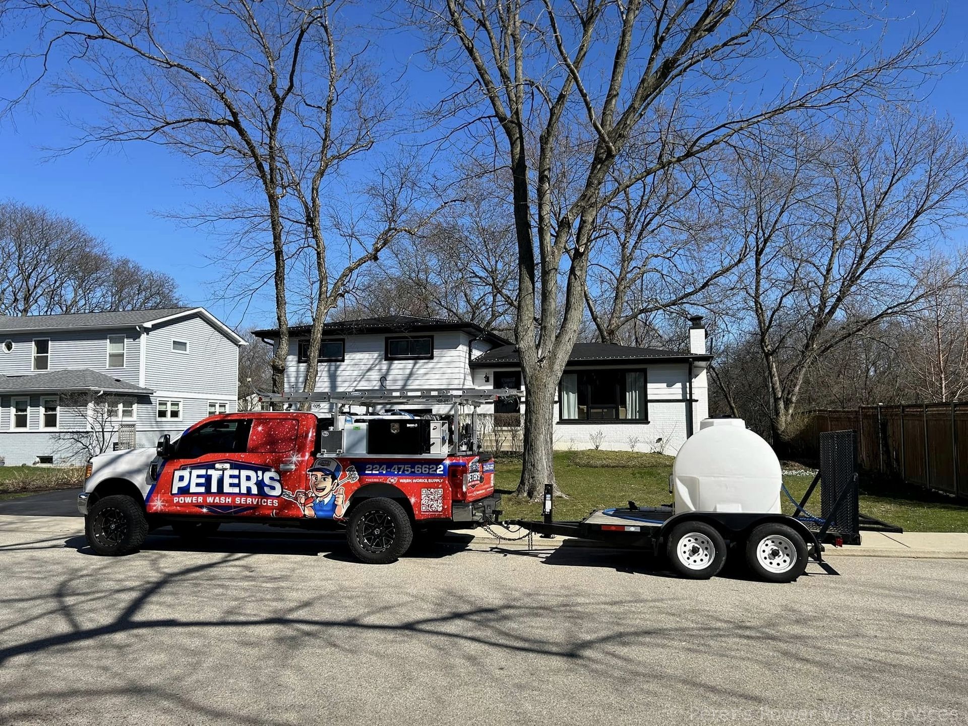 You can see an image of a Peter Power Washing truck and water tank trailer parked in a residential neighborhood during a Soft Washing service in Hoffman Estates, with homes, leafless trees, and a clear blue sky visible in the background.