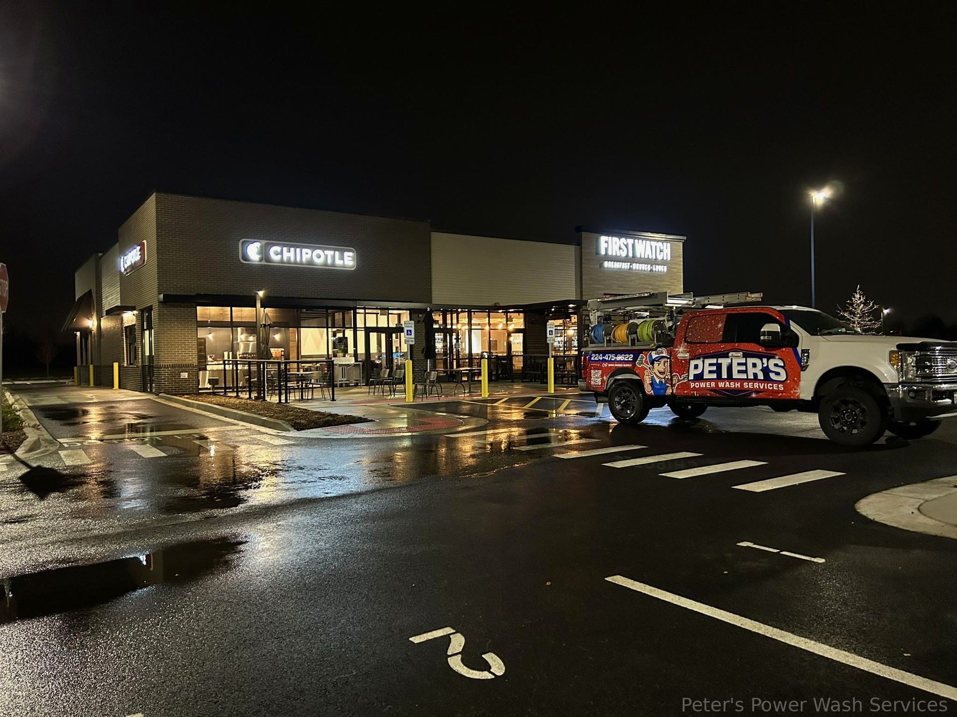Picture of a Peter Power Washing service truck parked outside a modern commercial building at night after Power Washing Companies work in Lincolnshire, with wet pavement reflecting lights from the storefront and parking lot.