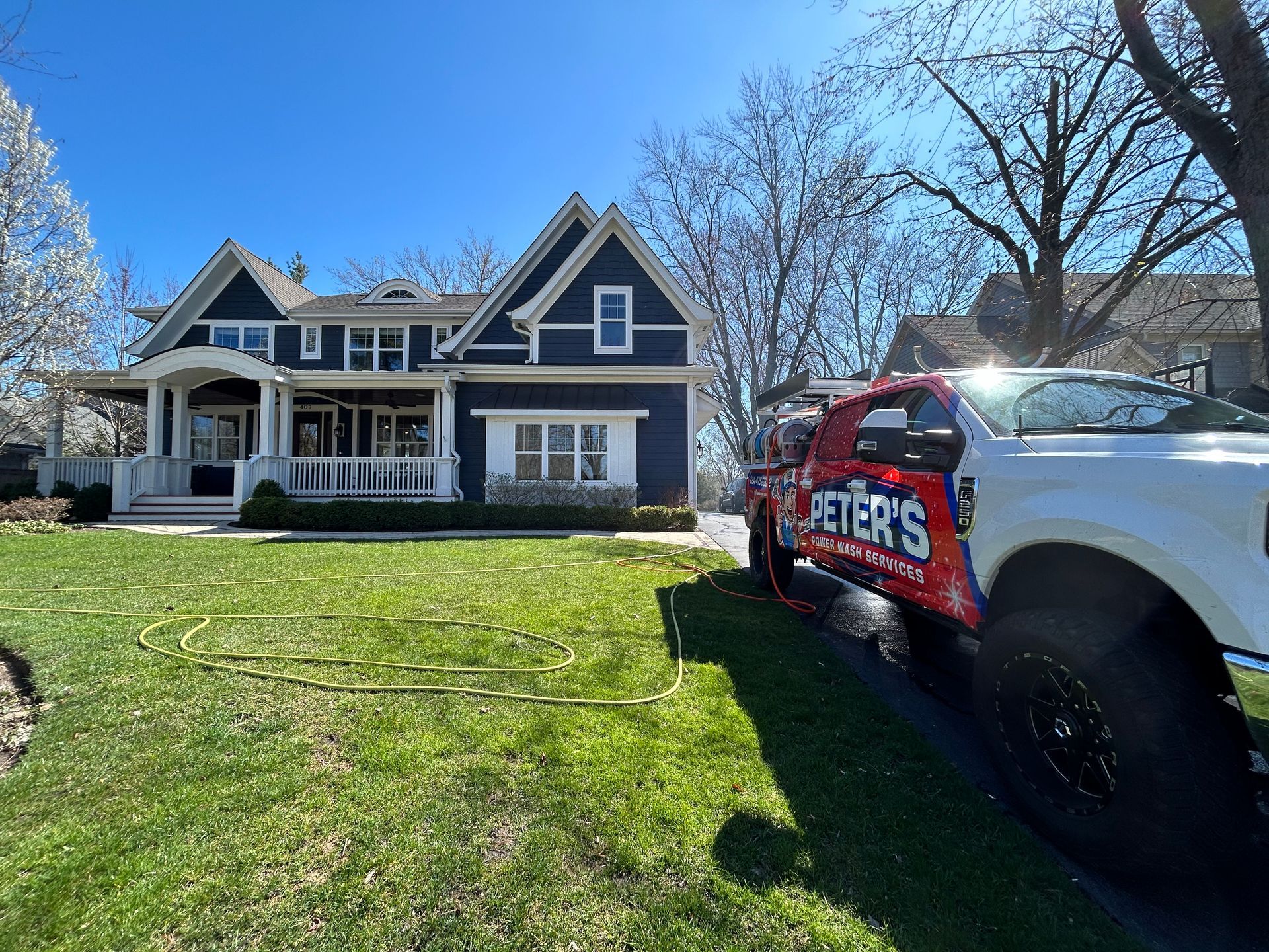 Image of a Peter Power Washing truck parked outside a residential property during a Soft Washing power washing service, showing freshly maintained grass, a large home, and cleaning equipment prepared for exterior washing.