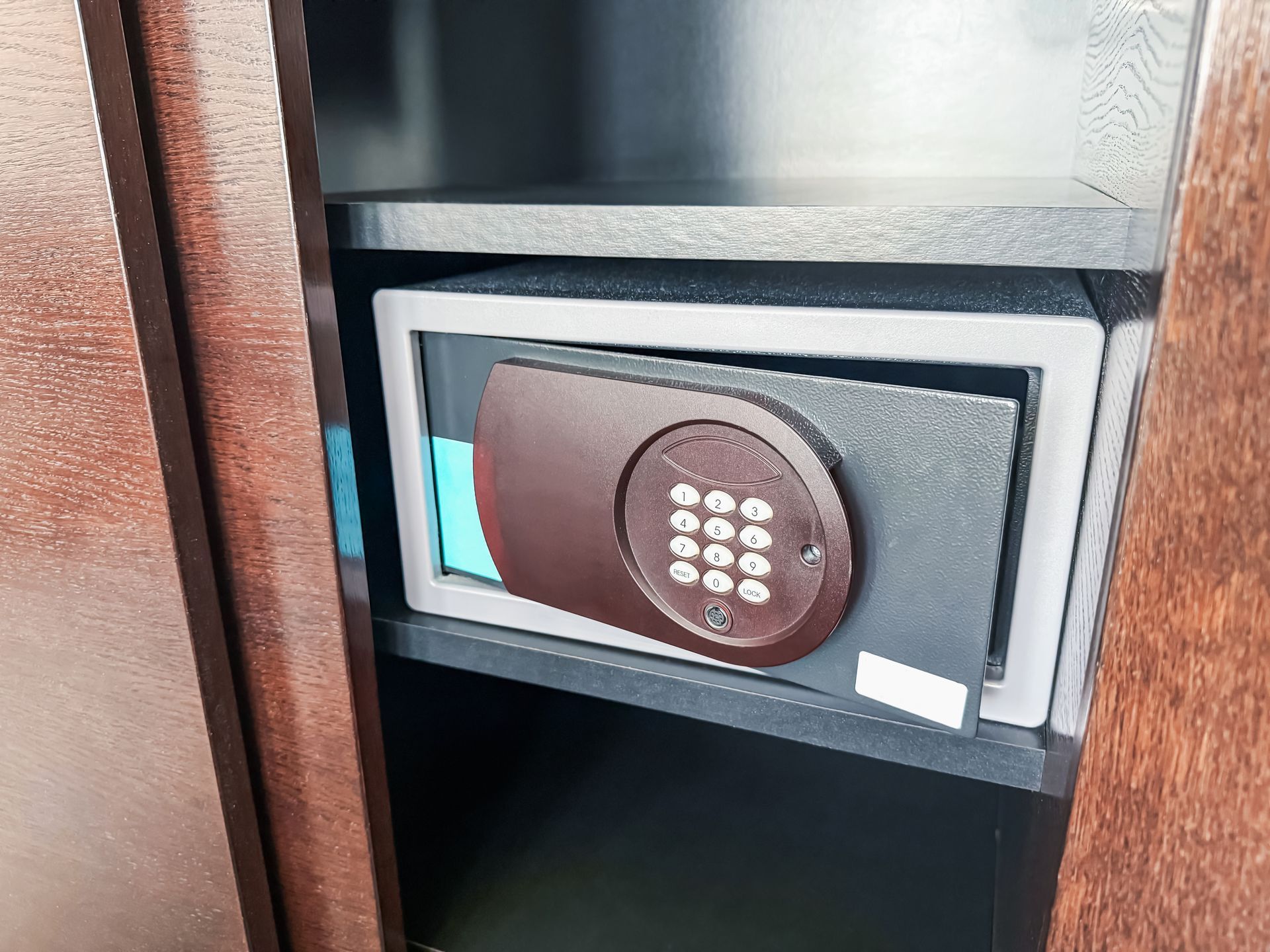 Keypad electronic safe inside a wooden cabinet shelf, with a brown circular lock panel.