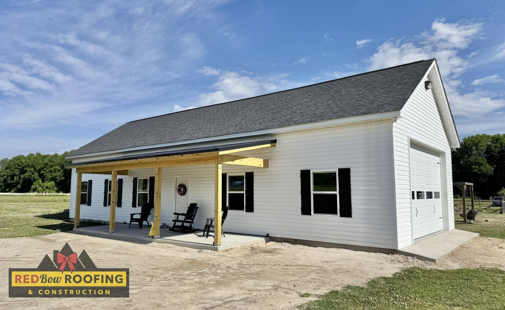White house with black shutters and gray roof under construction, with covered porch and grassy yard