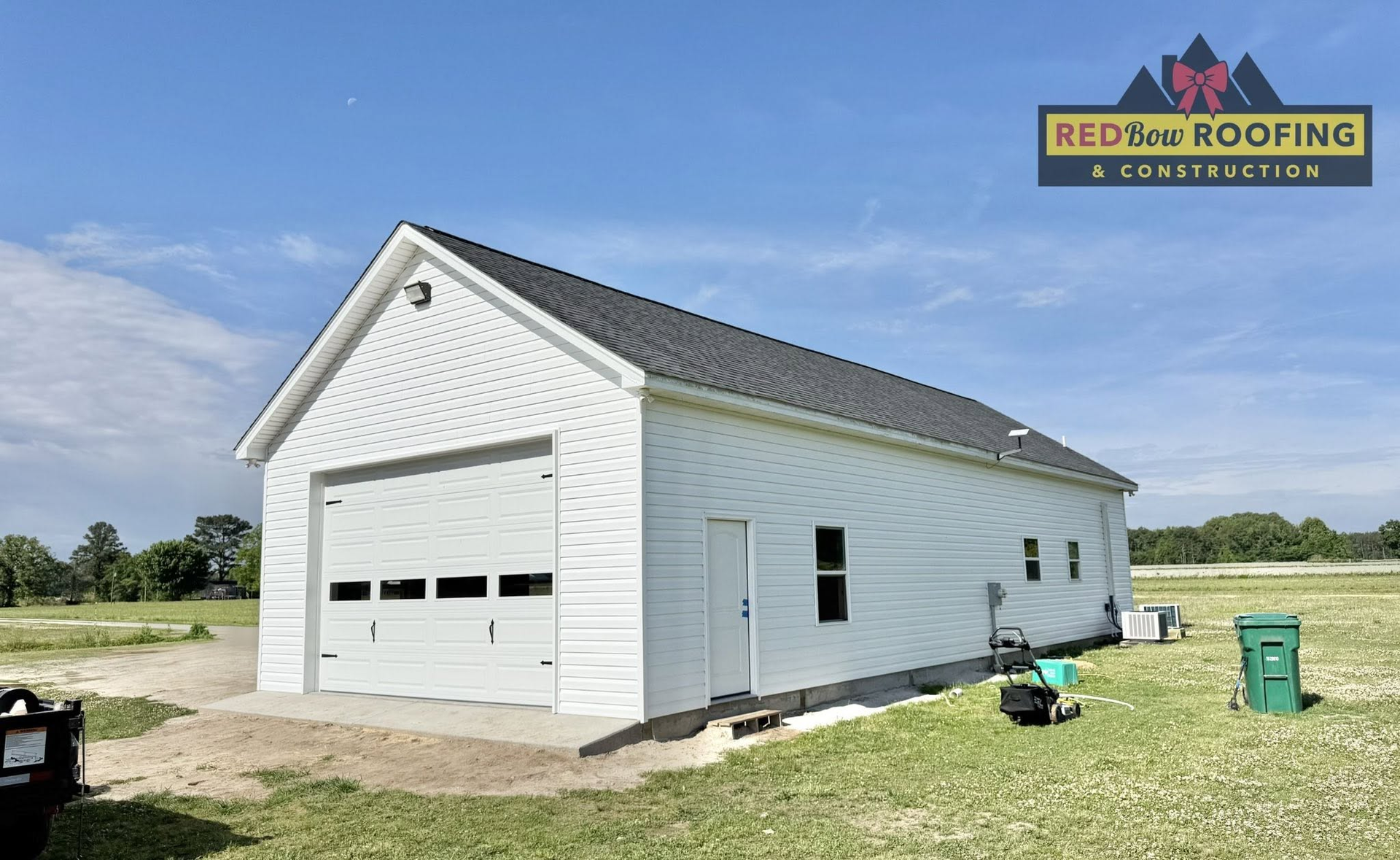 White garage with new roof and siding on a grassy lot under a blue sky, with roofing logo overlay