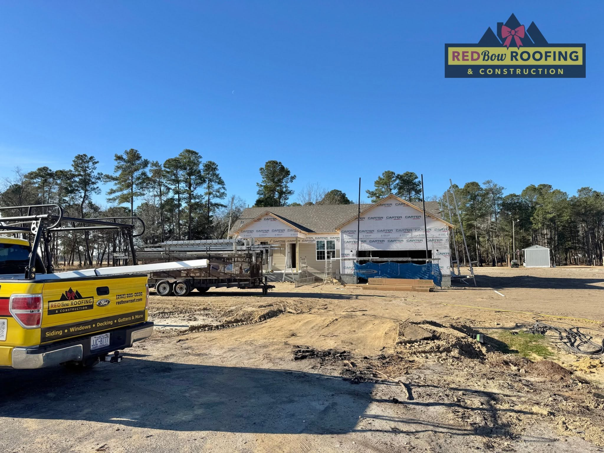 Roofing crew truck and materials at a house under construction, with a Red’s Roofing logo in the corner