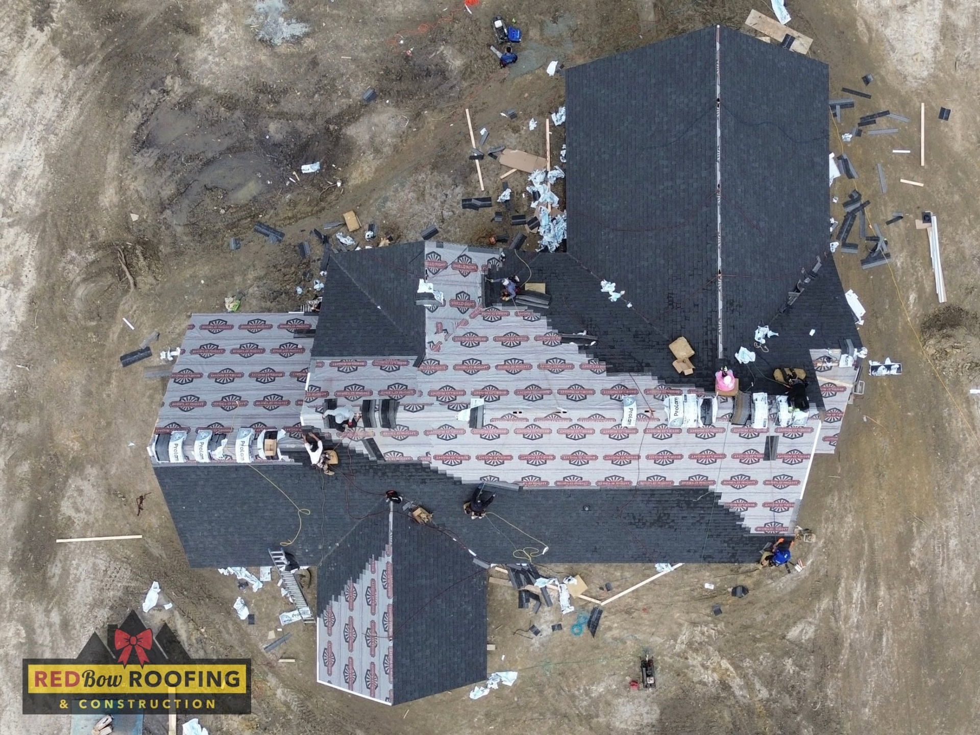 Aerial view of roof repair with workers on a house, exposed underlayment, and roofing materials scattered around.