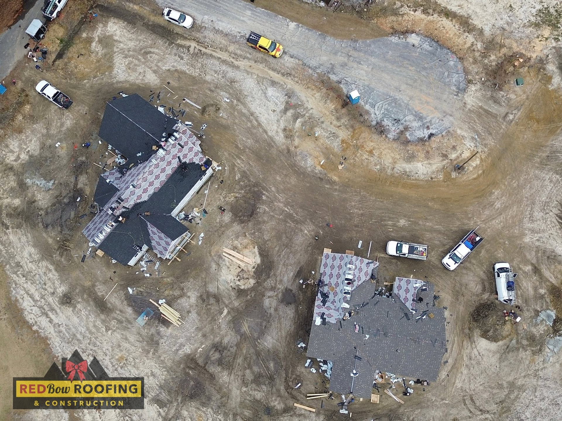 Aerial view of two damaged rooftops at a construction site with several parked vehicles nearby.
