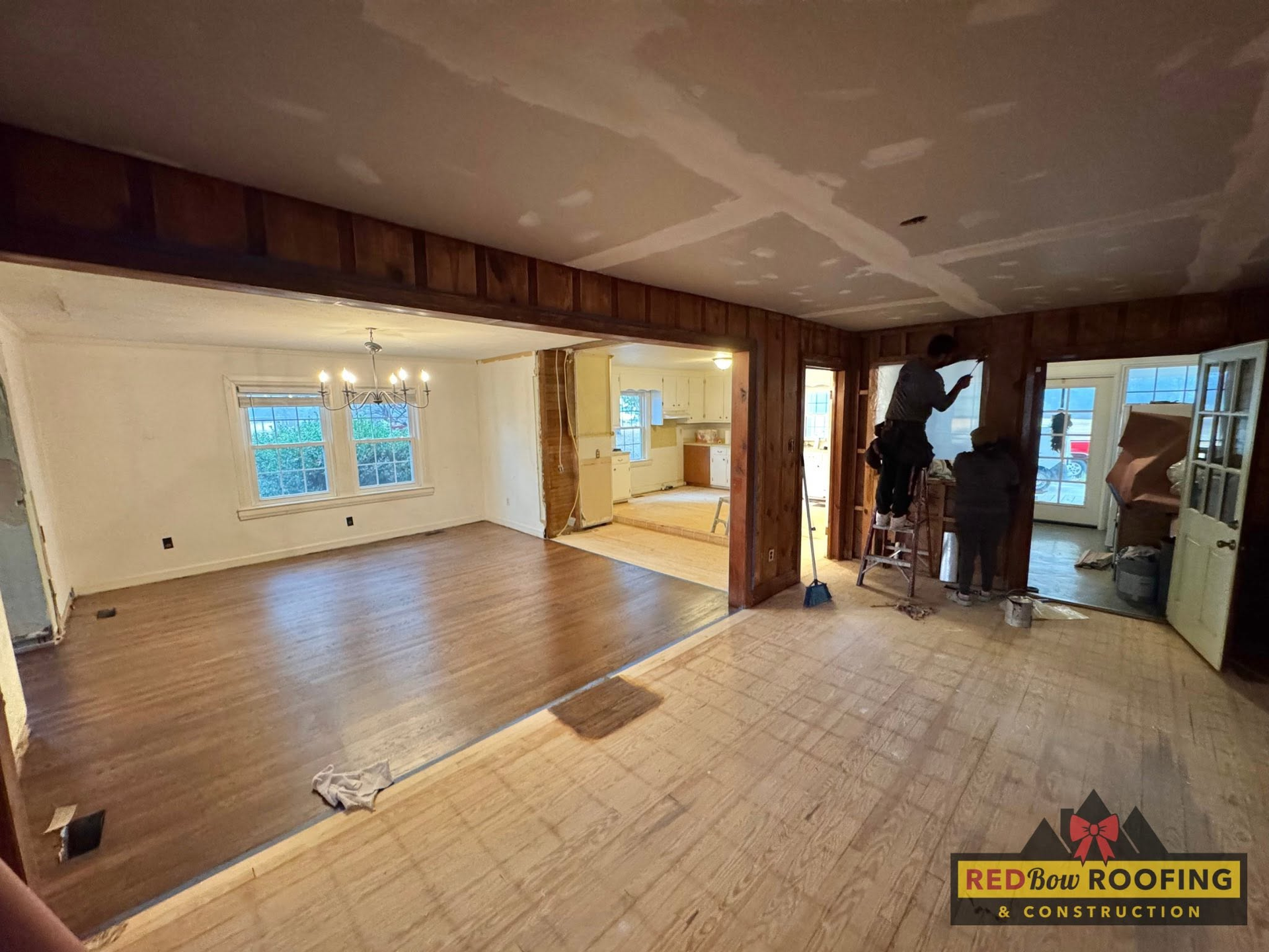 Renovated interior room with wood floors, exposed framing, and a partially open wall to a kitchen area