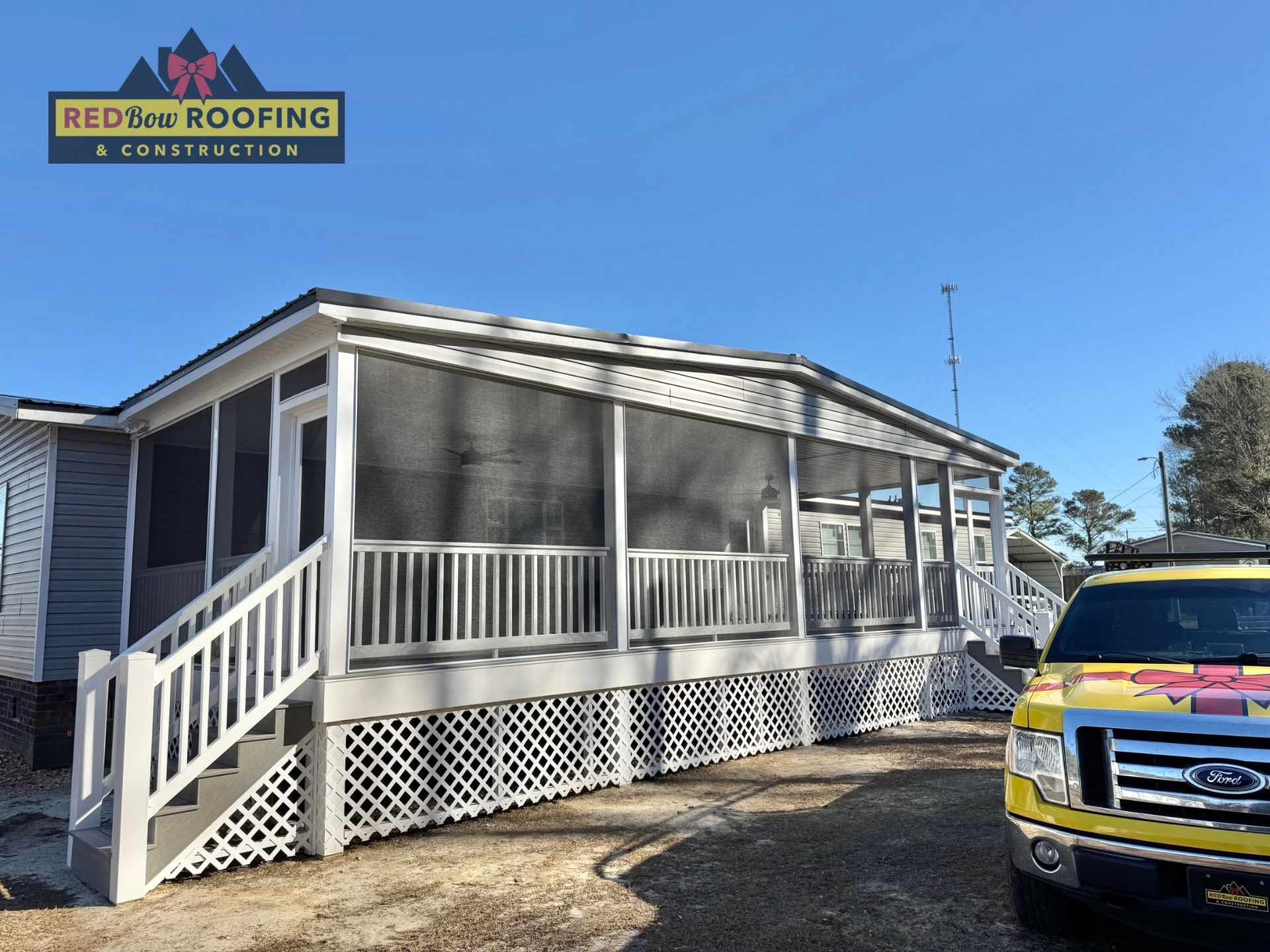 White house with screened porch and ramp, with a yellow work truck in the driveway under a clear blue sky