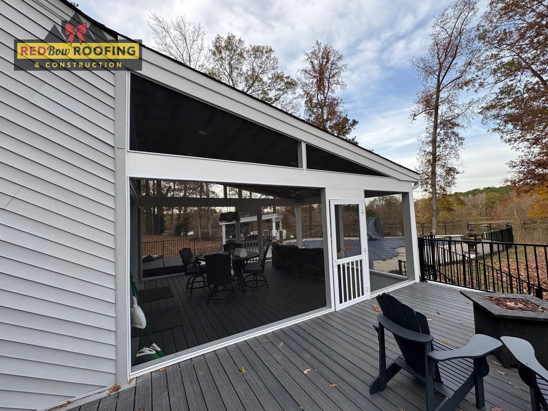 Screened porch with black table and chairs on a gray house deck, overlooking a wooded yard