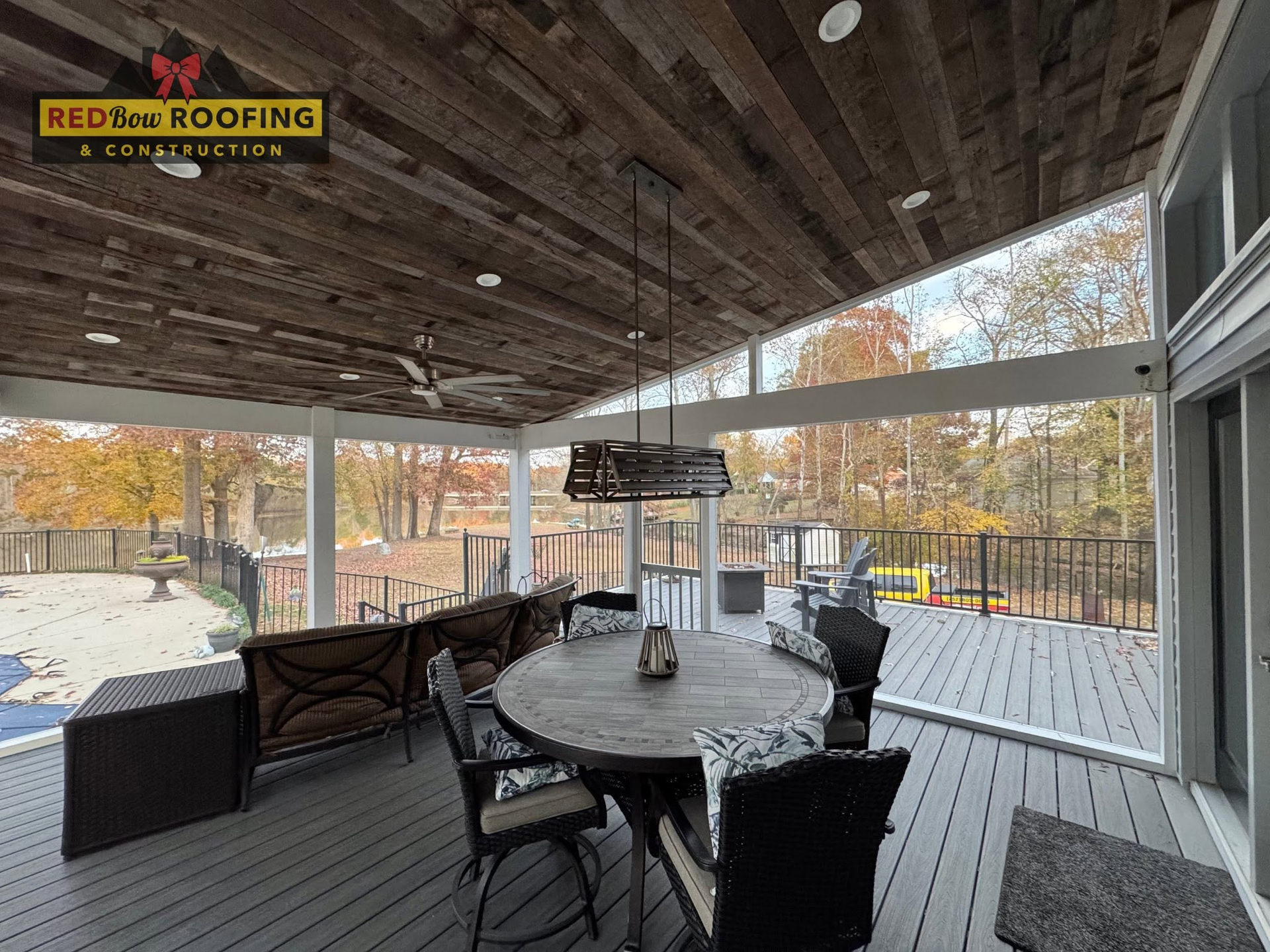 Covered deck with dining table and chairs overlooking an autumn yard, with a patio heater and outdoor seating.