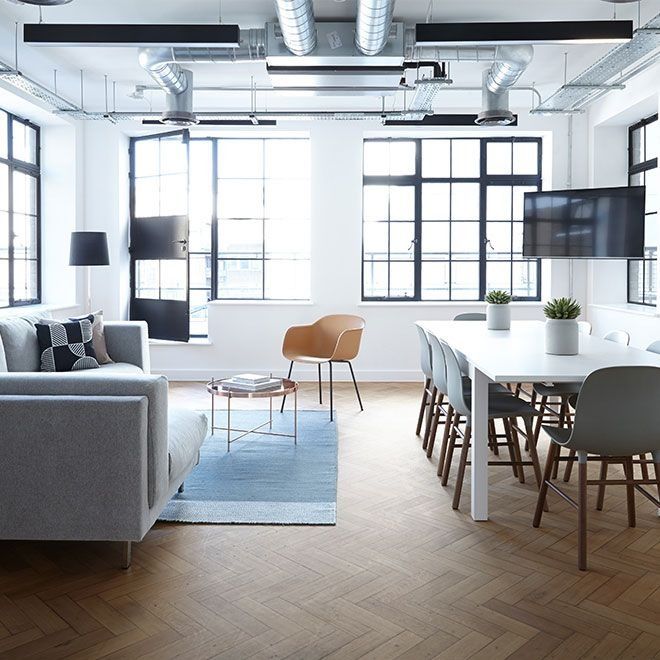 Bright office interior with a sofa, table, chairs, and large windows.