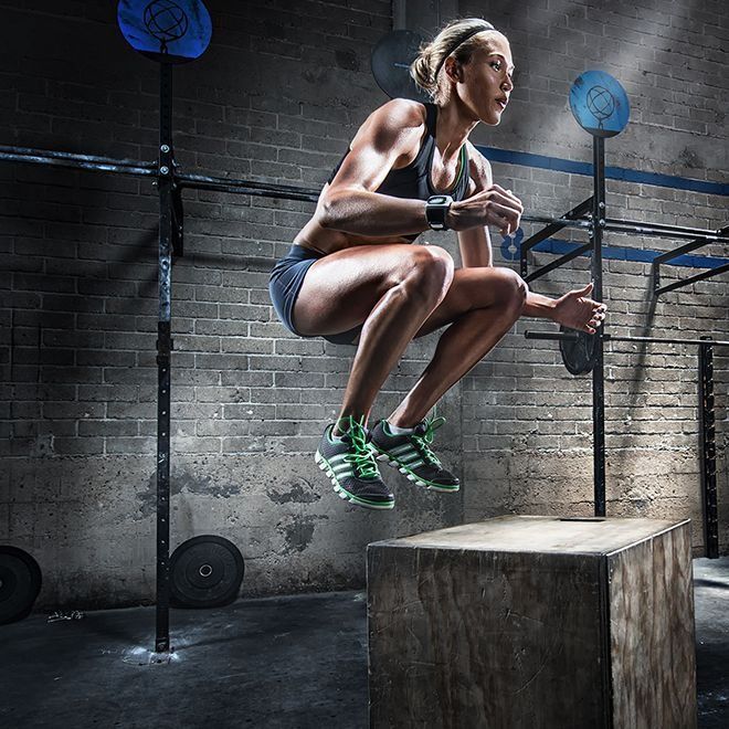 Woman in athletic wear performing a box jump in a gym.