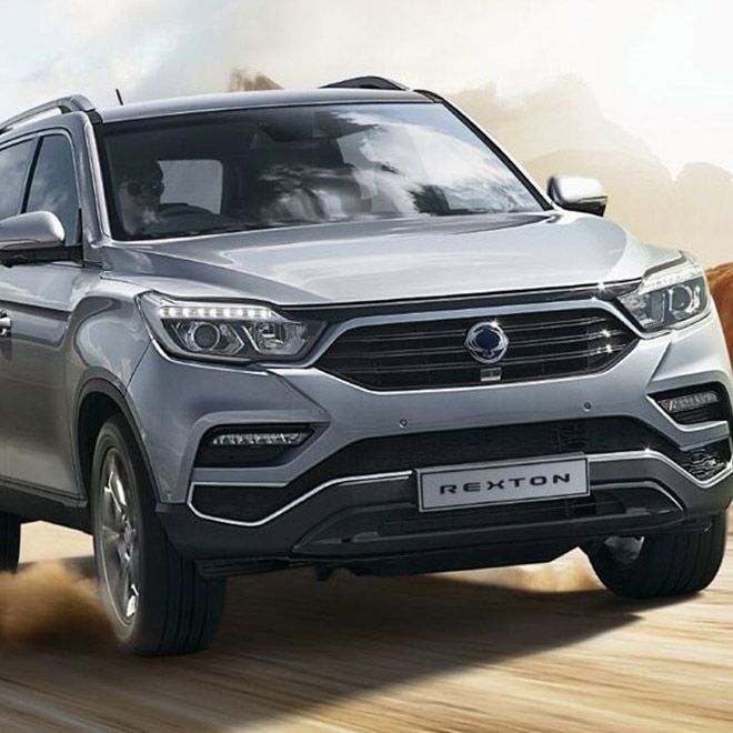 Silver SsangYong Rexton SUV driving on a dirt road, angled view.