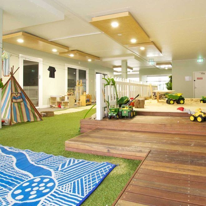 Playroom with artificial grass, wooden platform, sand pit, and toys.