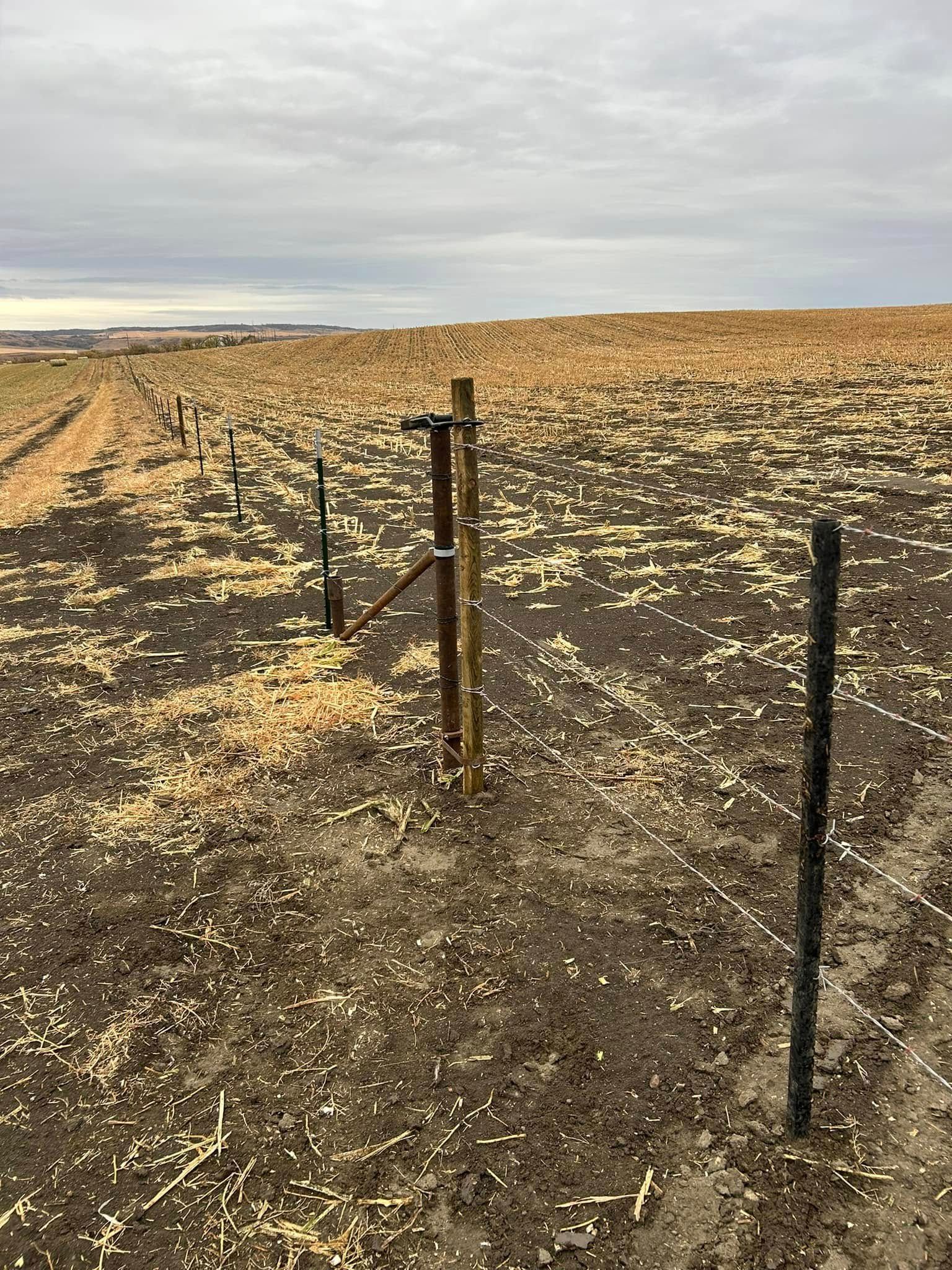 A brown field with a partially constructed fence under a cloudy sky.