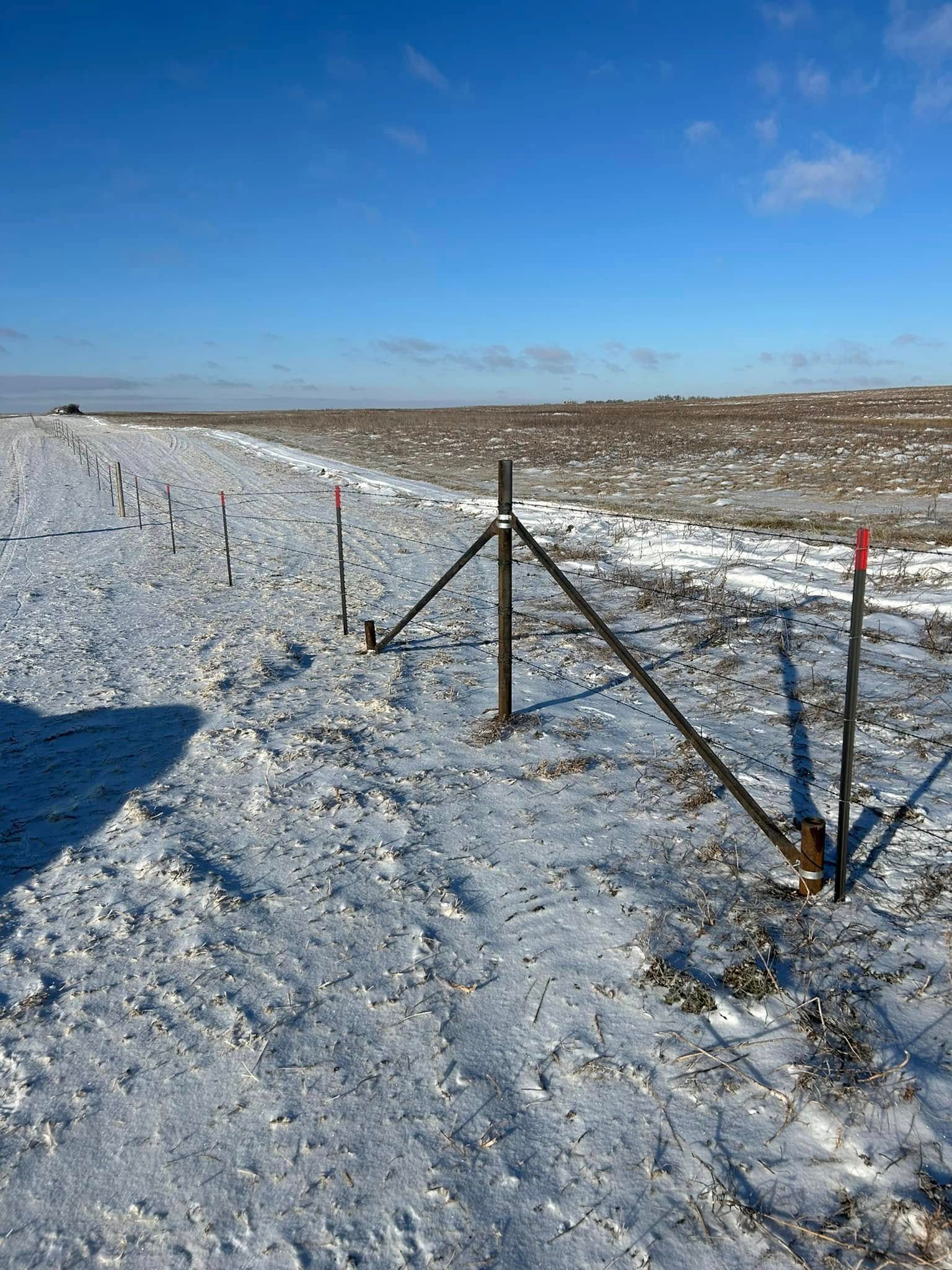 Snowy field with surveyor's stakes and a wooden structure under a blue sky.