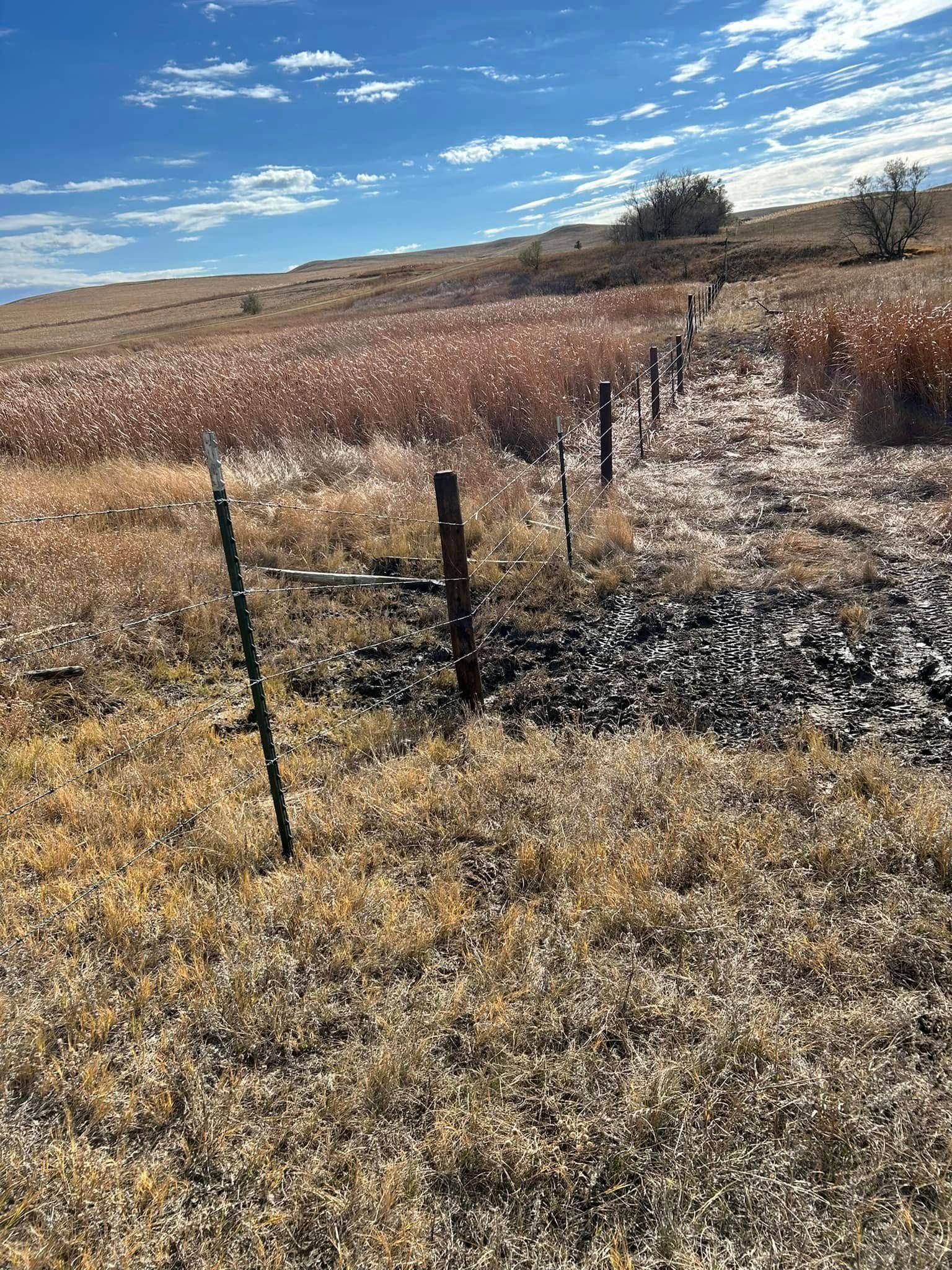 Brown grass field with a fence line, leading up to a hillside under a blue sky.