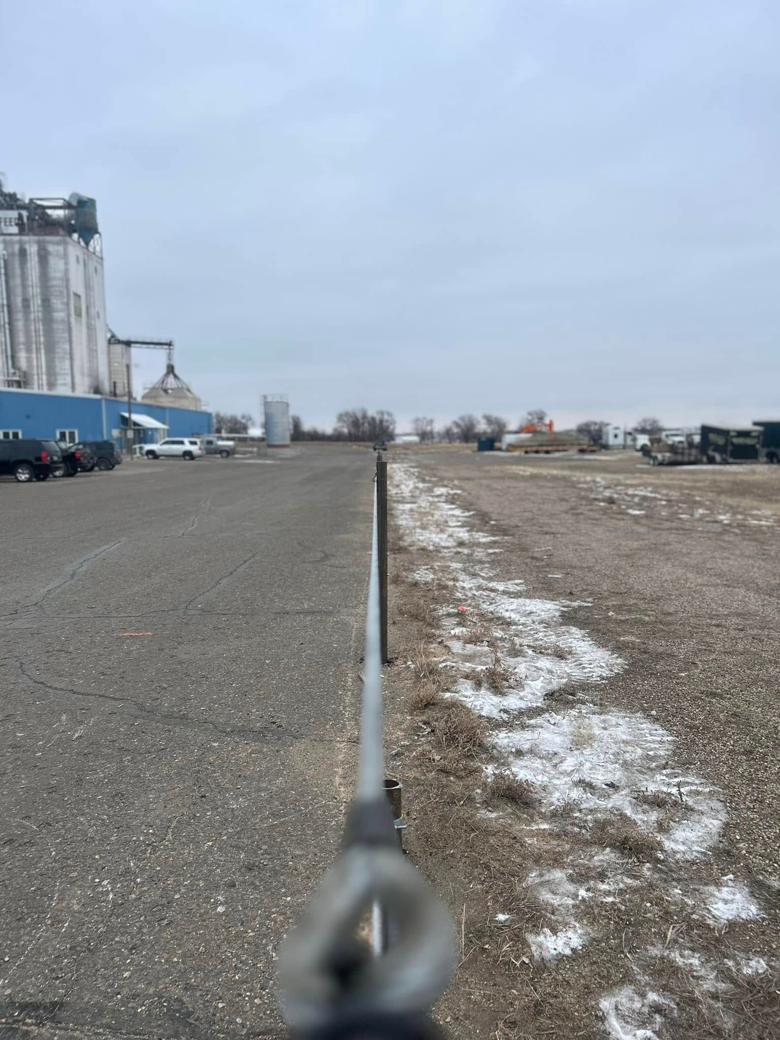 Gravel parking lot with buildings in the distance and a gray sky. Snow patches are present.