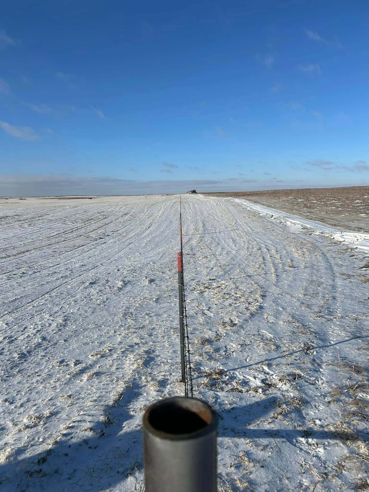 A snowy field with a black cylinder and metal structure in the foreground, against a clear blue sky.