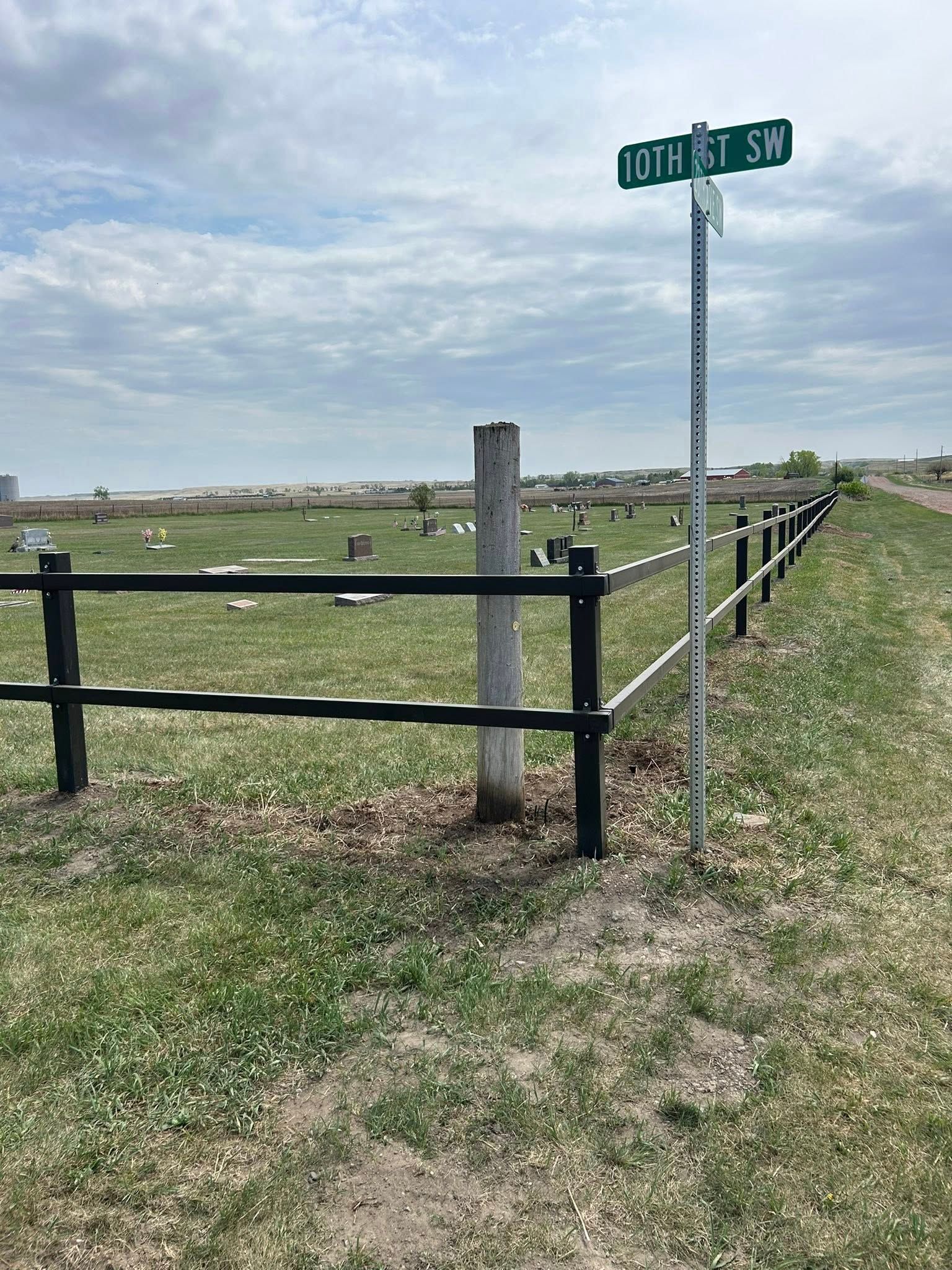 Cemetery with a black and silver fence, street sign, and cloudy sky.