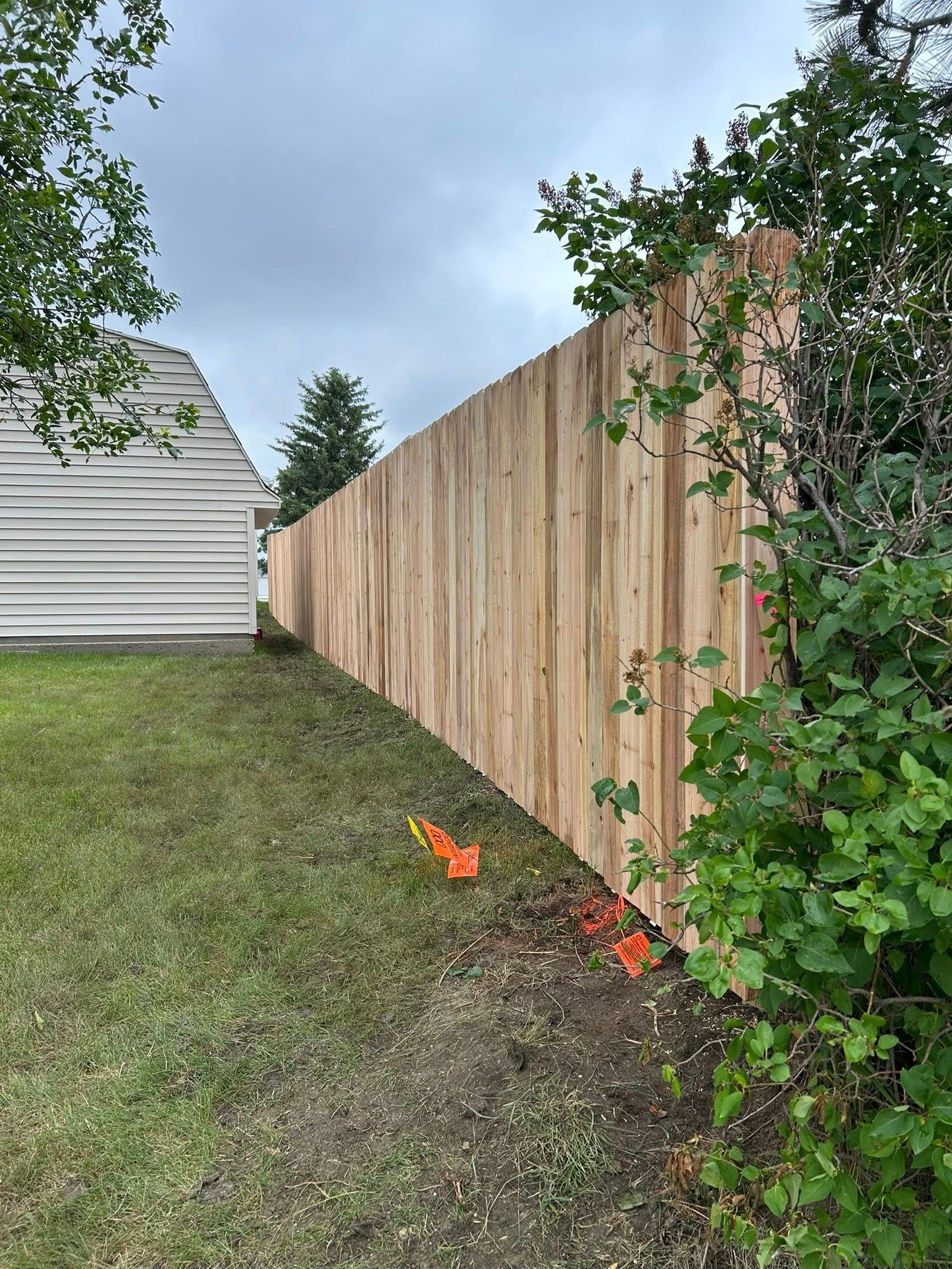 Wooden fence in a grassy yard, under a cloudy sky. Orange flags near the fence.