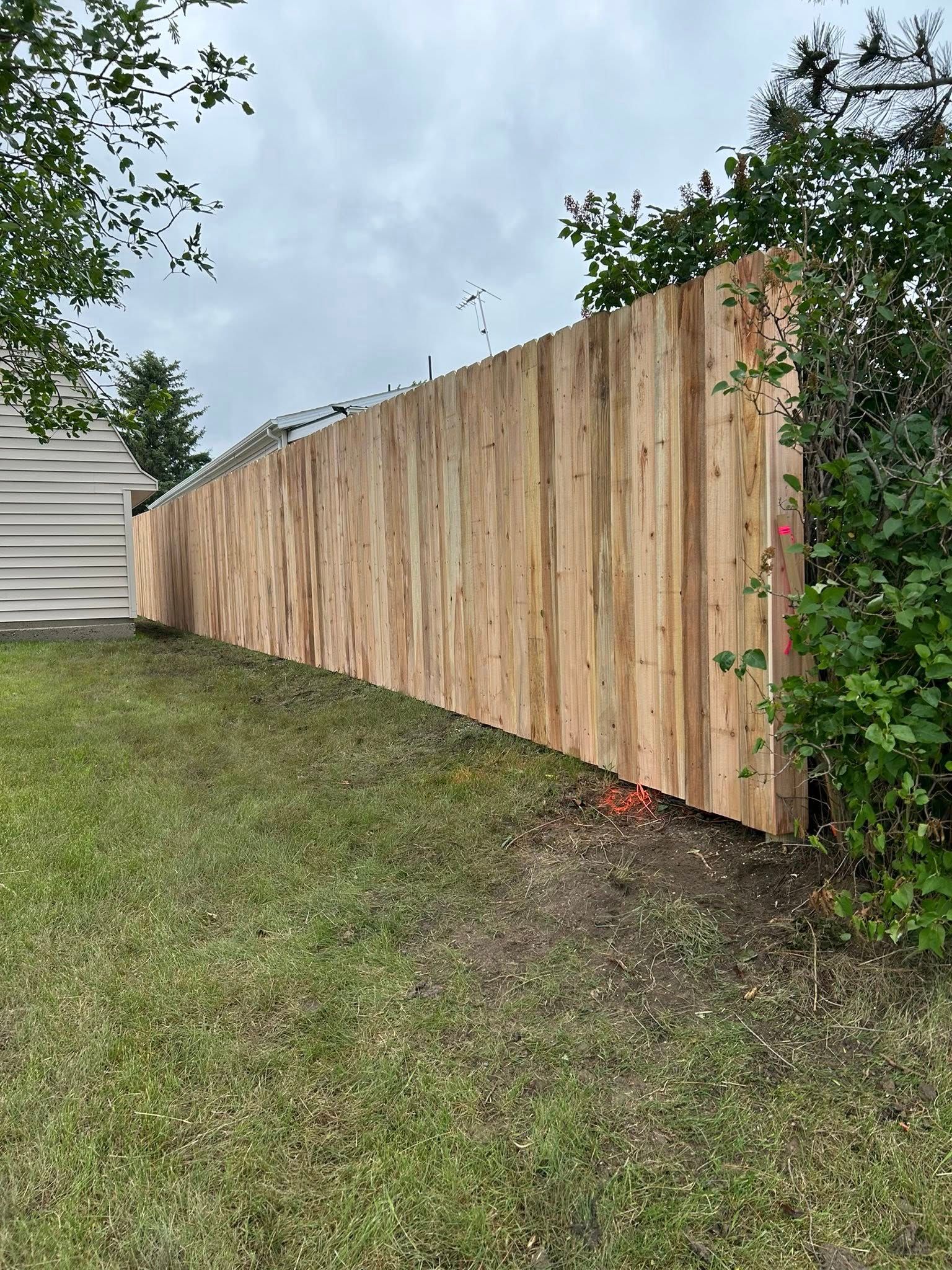 Wooden fence on a slight incline, with grass in the foreground and a house on the left.