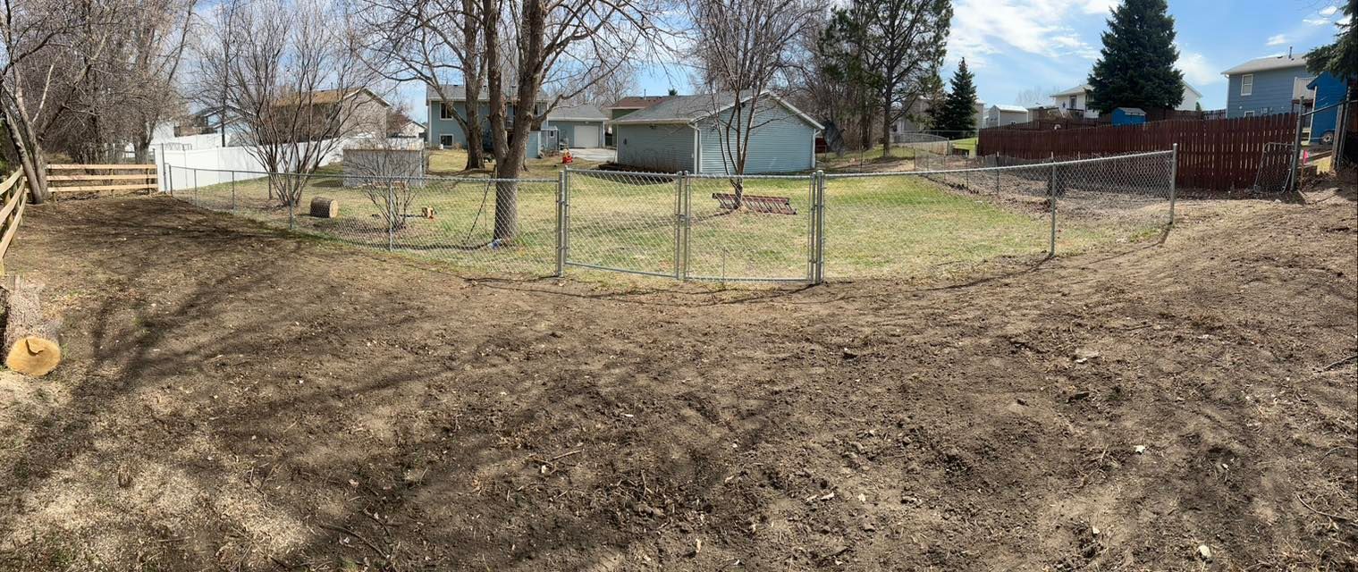 A wide, brown, cleared yard with a short fence in the middle, small house in the background.