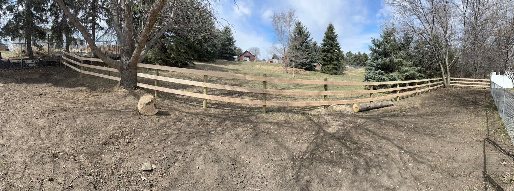 A split-rail fence follows the contour of a grassy hill under a blue sky.