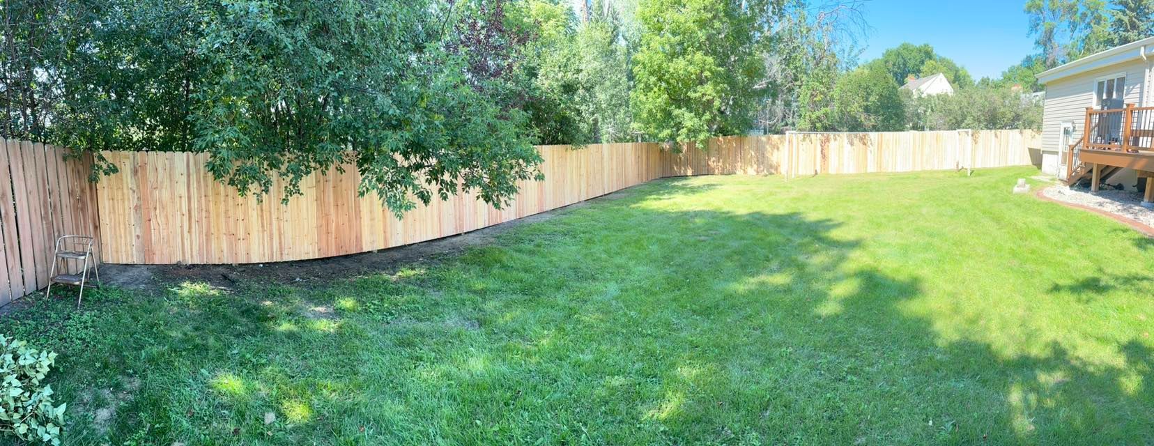 A fenced-in backyard with green grass and trees. A wood deck is visible on the right.